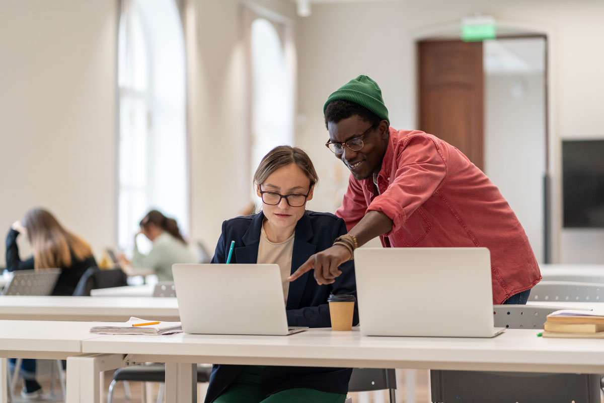 African american guy helps caucasian girl students working on project in college university.